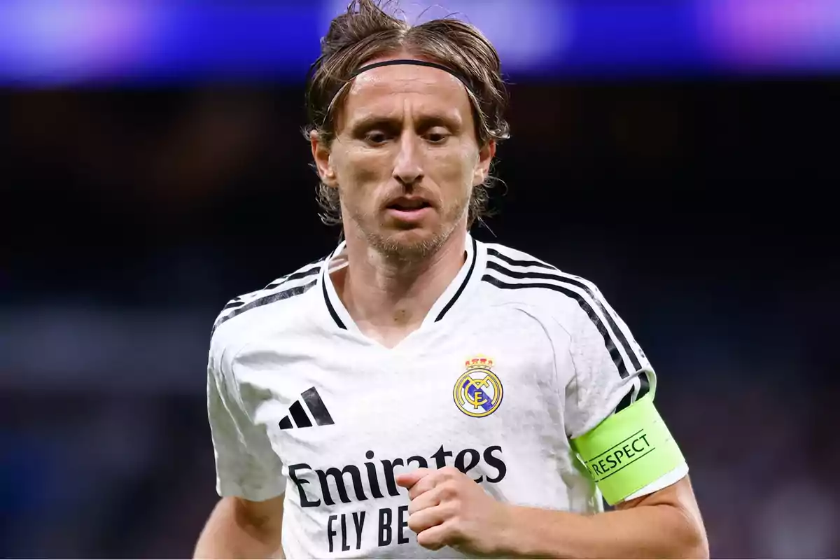 Un jugador de fútbol con uniforme blanco y brazalete verde en el campo.