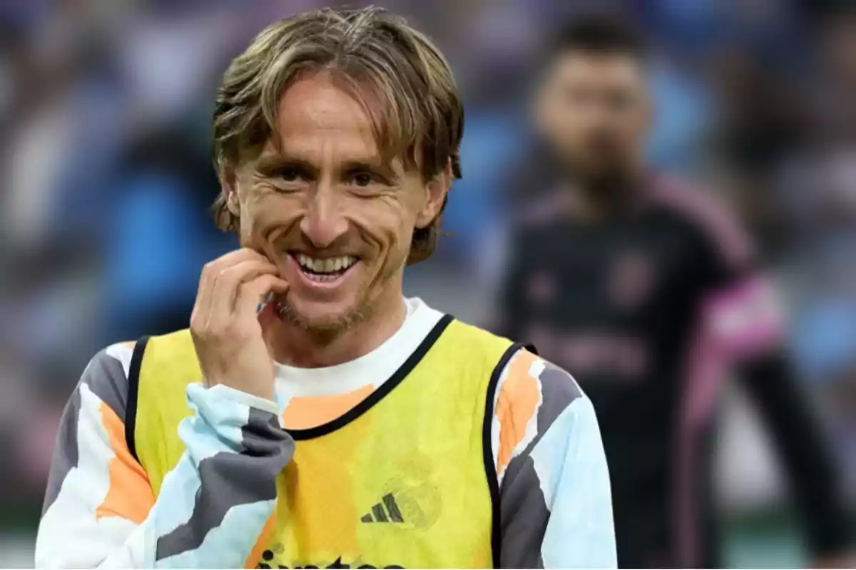 Un jugador de fútbol sonríe mientras lleva un peto amarillo sobre su uniforme deportivo en un estadio.
