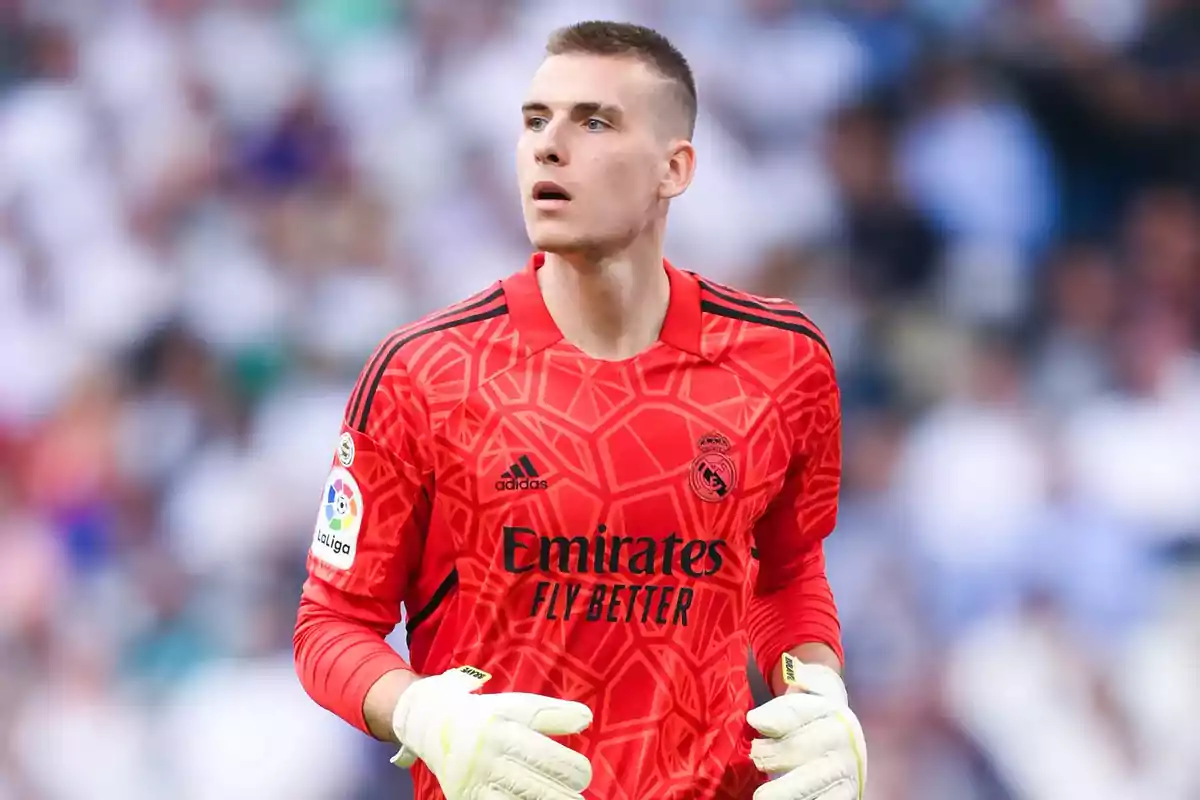 A soccer player in a red goalkeeper uniform and white gloves in a stadium. A soccer player in a red goalkeeper uniform and white gloves in a stadium.