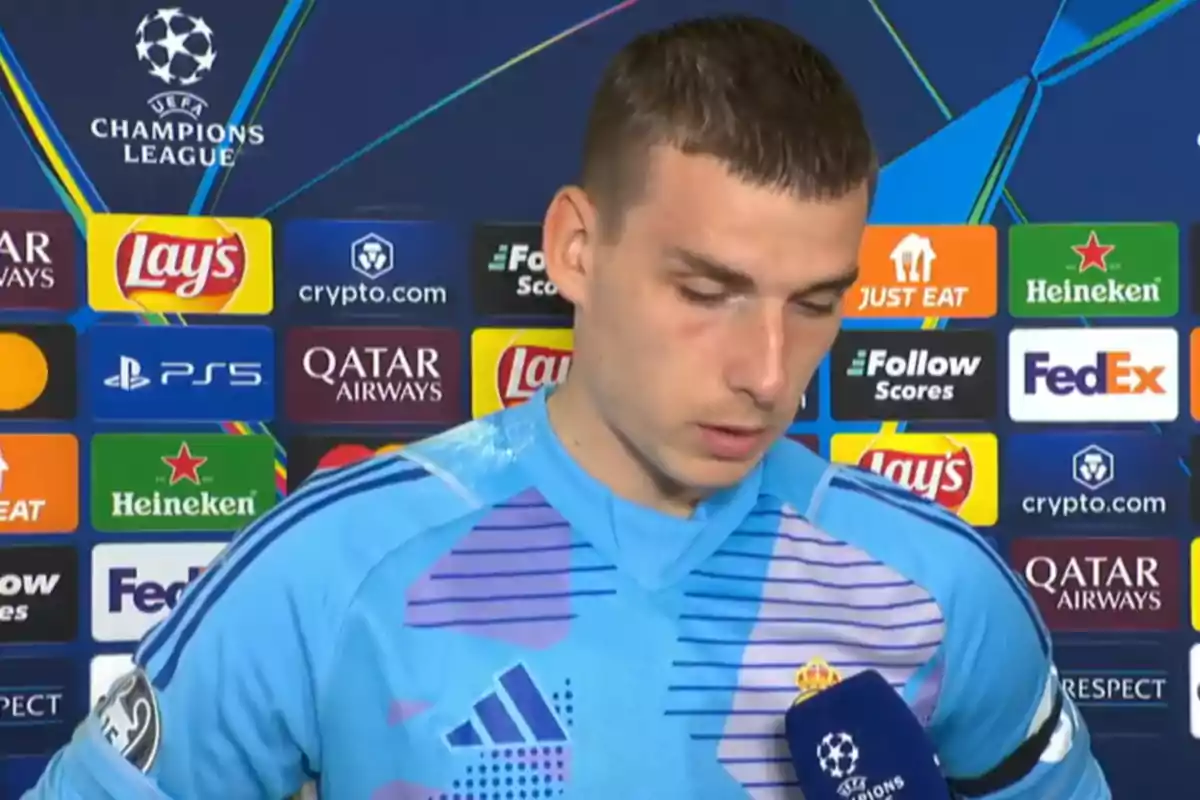 A soccer player in a light blue uniform is being interviewed in front of a panel with logos of UEFA Champions League sponsors. A soccer player in a light blue uniform is being interviewed in front of a panel with logos of UEFA Champions League sponsors.