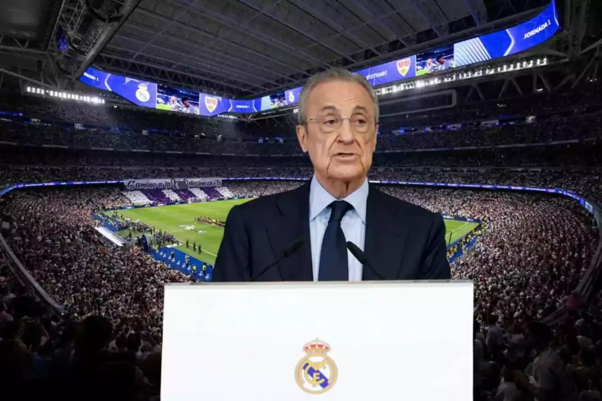 Un hombre de traje hablando en un podio con el logo del Real Madrid en un estadio lleno de espectadores.