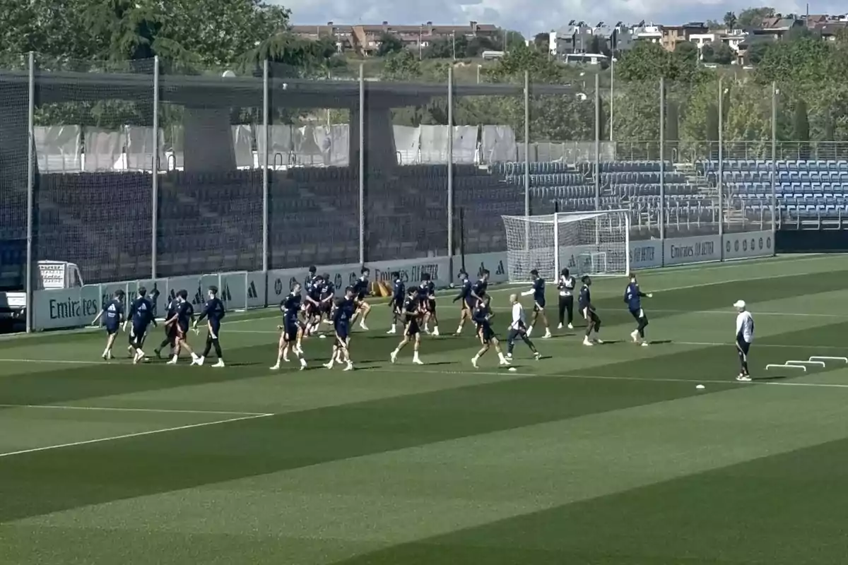 Un grupo de personas entrenando en un campo de fútbol con gradas vacías al fondo y un entrenador observando. Un grupo de personas entrenando en un campo de fútbol con gradas vacías al fondo y un entrenador observando.