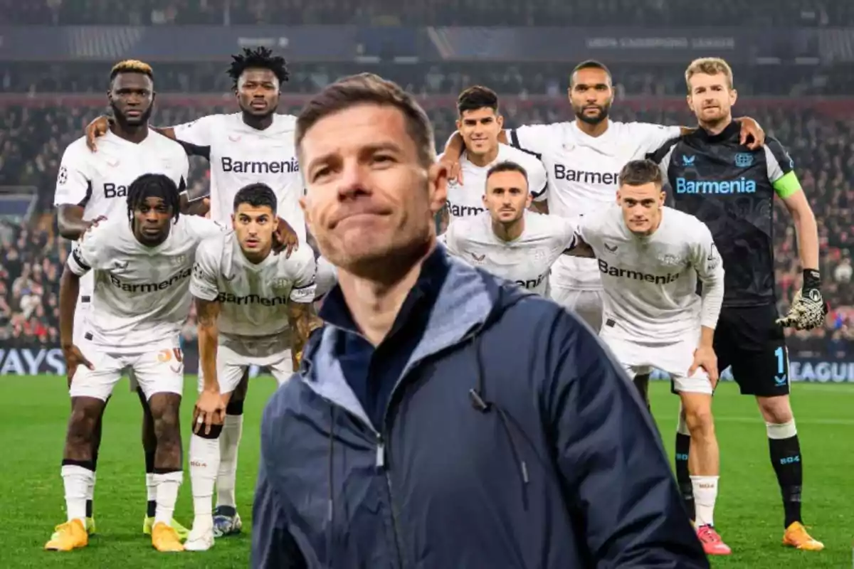 Un grupo de jugadores de fútbol con uniformes blancos posan en el campo mientras un hombre con chaqueta oscura está en primer plano.