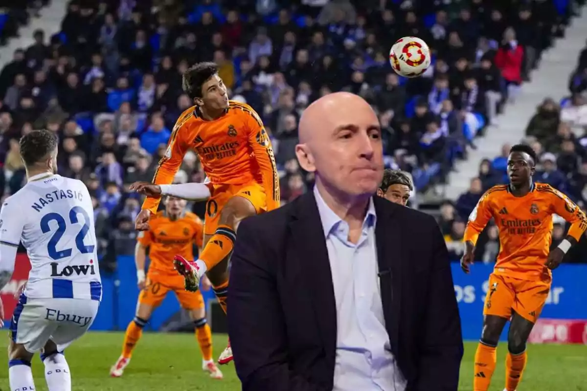 A player in an orange uniform jumps to head the ball while another player from the opposing team watches; in the foreground, a bald man in a dark suit.