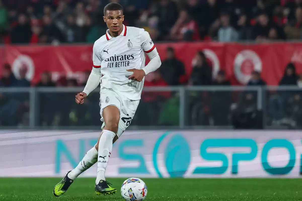 Un jugador de fútbol con uniforme blanco controla el balón en el campo durante un partido.