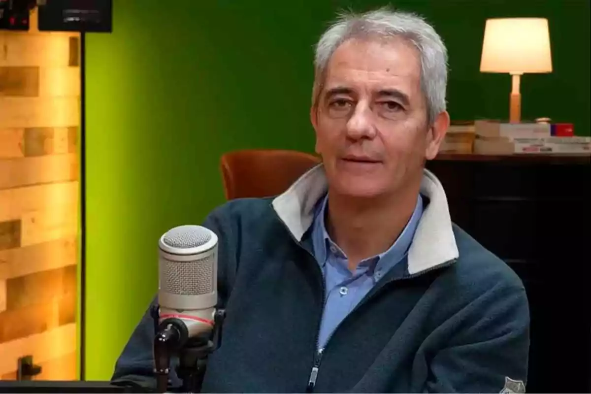 Hombre de cabello canoso sentado frente a un micrófono en un estudio con fondo verde y una lámpara encendida. Hombre de cabello canoso sentado frente a un micrófono en un estudio con fondo verde y una lámpara encendida.