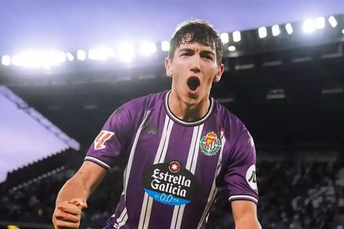 Jugador de fútbol con uniforme morado celebrando en un estadio iluminado.