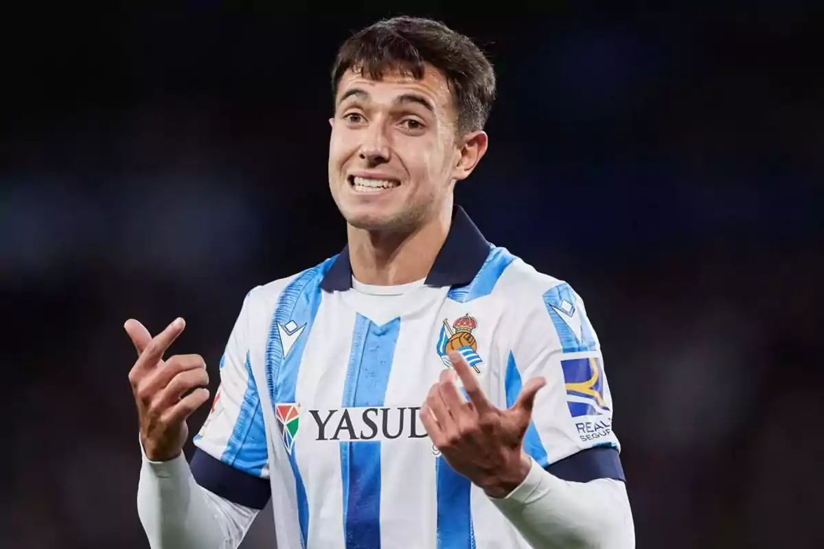 Un jugador de fútbol con uniforme blanco y azul gesticula con las manos durante un partido. Un jugador de fútbol con uniforme blanco y azul gesticula con las manos durante un partido.