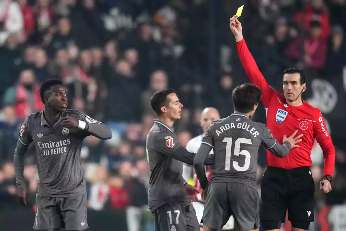 A referee shows a yellow card to a player during a soccer match while other players watch the situation. A referee shows a yellow card to a player during a soccer match while other players watch the situation.
