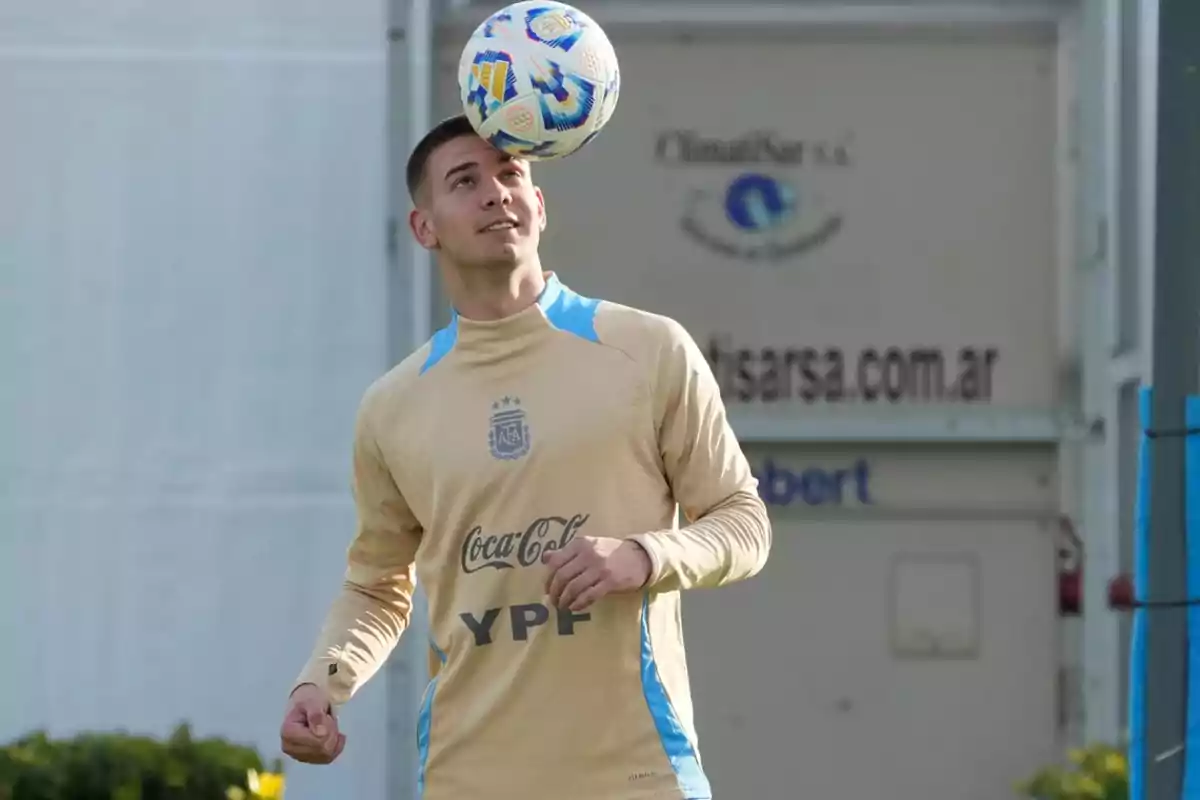 Futbolista con uniforme de entrenamiento beige de la selección argentina haciendo dominio de balón con la cabeza en una cancha al aire libre Futbolista con uniforme de entrenamiento beige de la selección argentina haciendo dominio de balón con la cabeza en una cancha al aire libre