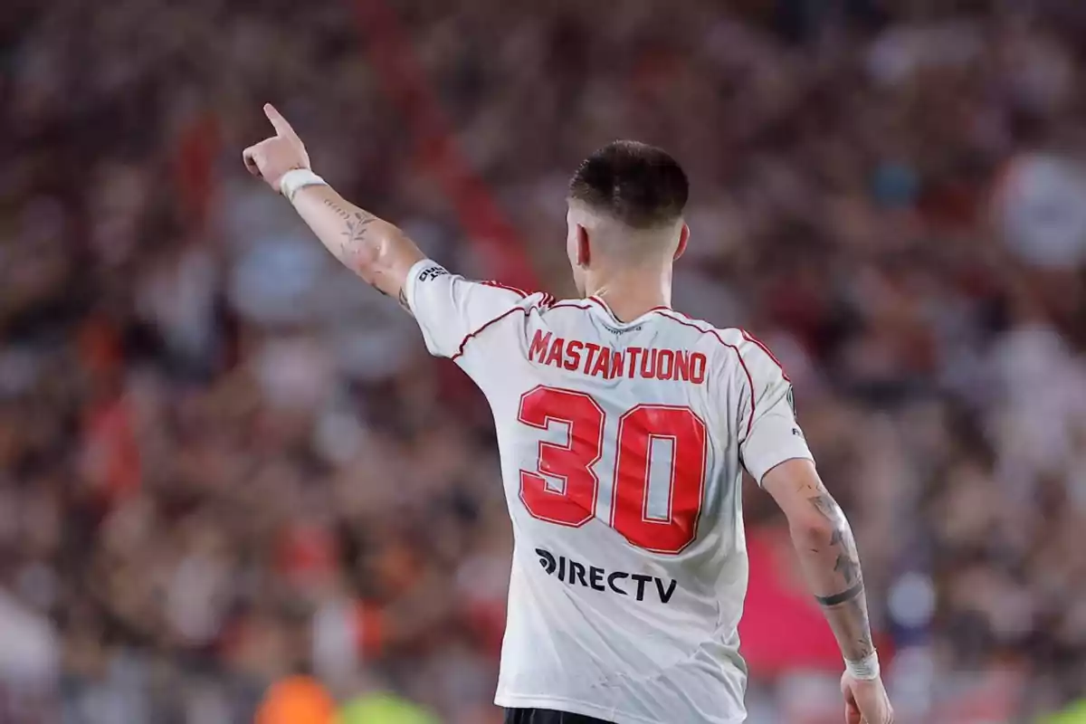 Soccer player wearing River Plate’s number 30 jersey pointing toward the sky in a packed stadium Soccer player wearing River Plate’s number 30 jersey pointing toward the sky in a packed stadium