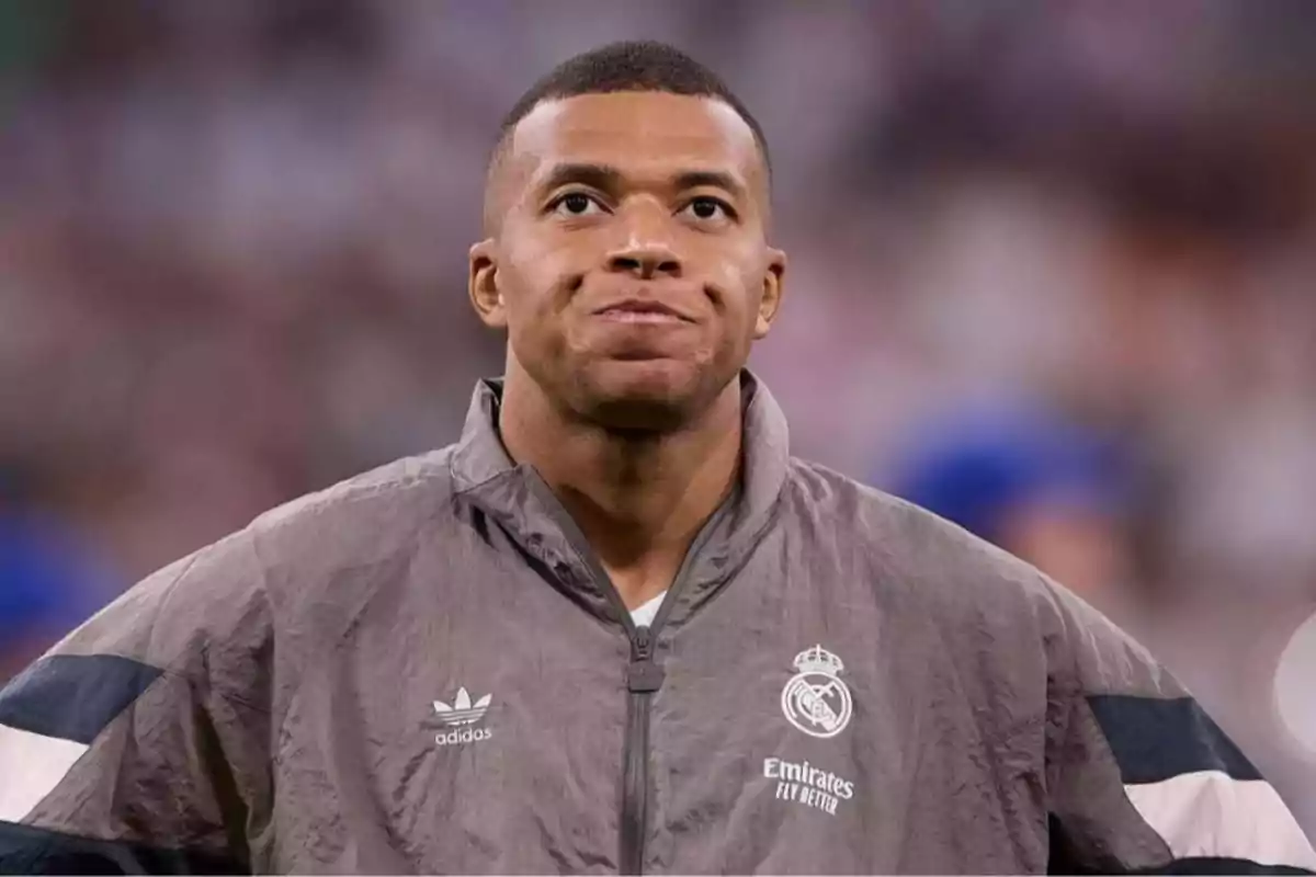 Jugador de fútbol con chaqueta gris del Real Madrid y expresión seria en un estadio Jugador de fútbol con chaqueta gris del Real Madrid y expresión seria en un estadio