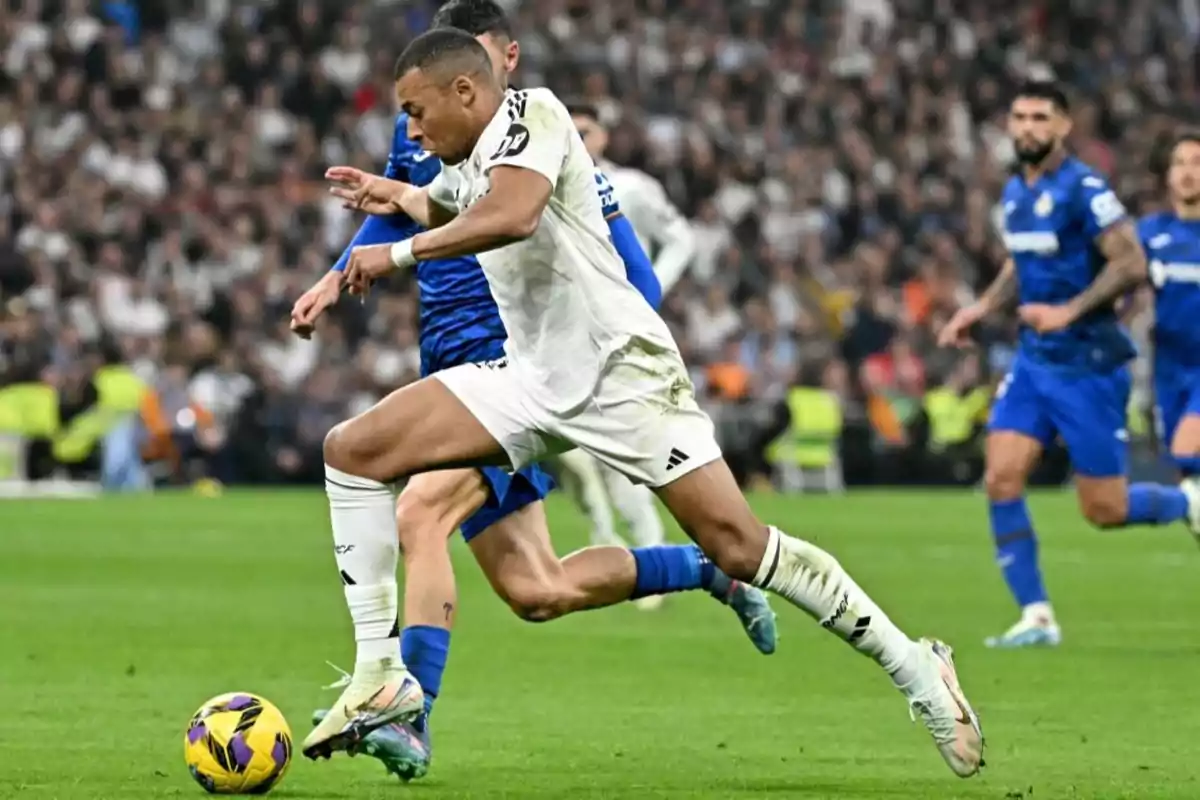 Soccer player in action during a match with the ball at his feet and other players around in a stadium full of spectators.