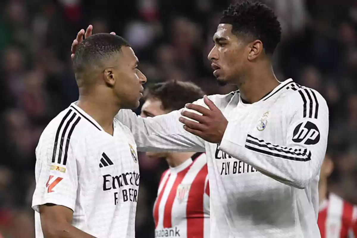 Dos jugadores de fútbol con uniformes blancos se saludan en el campo durante un partido.