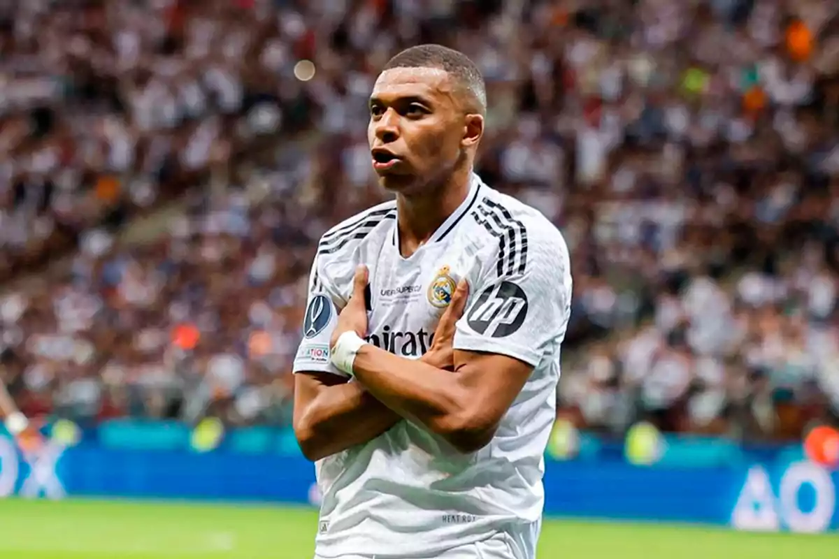 Un jugador de fútbol con uniforme blanco celebra en el campo con los brazos cruzados sobre el pecho. Un jugador de fútbol con uniforme blanco celebra en el campo con los brazos cruzados sobre el pecho.