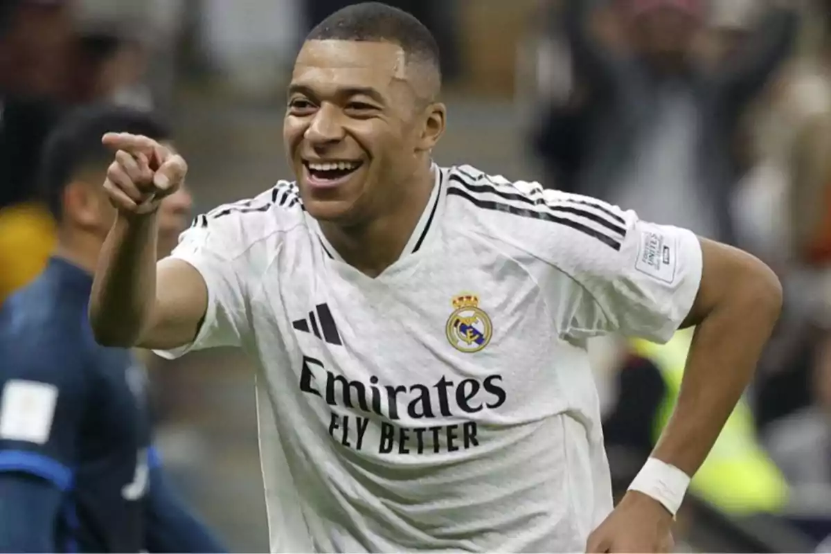 A soccer player smiles and points while wearing a white Real Madrid jersey at a match. A soccer player smiles and points while wearing a white Real Madrid jersey at a match.