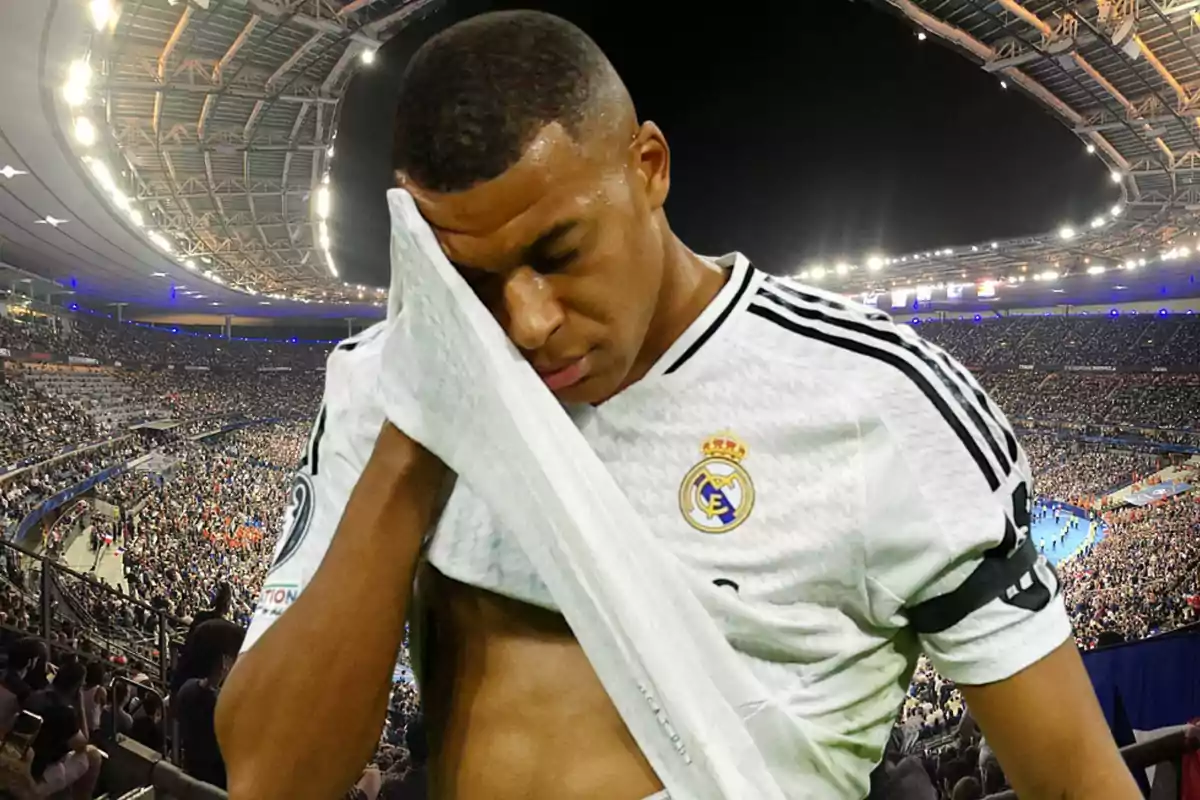 Soccer player wearing a white Real Madrid jersey wiping his face with his jersey in a stadium full of spectators
