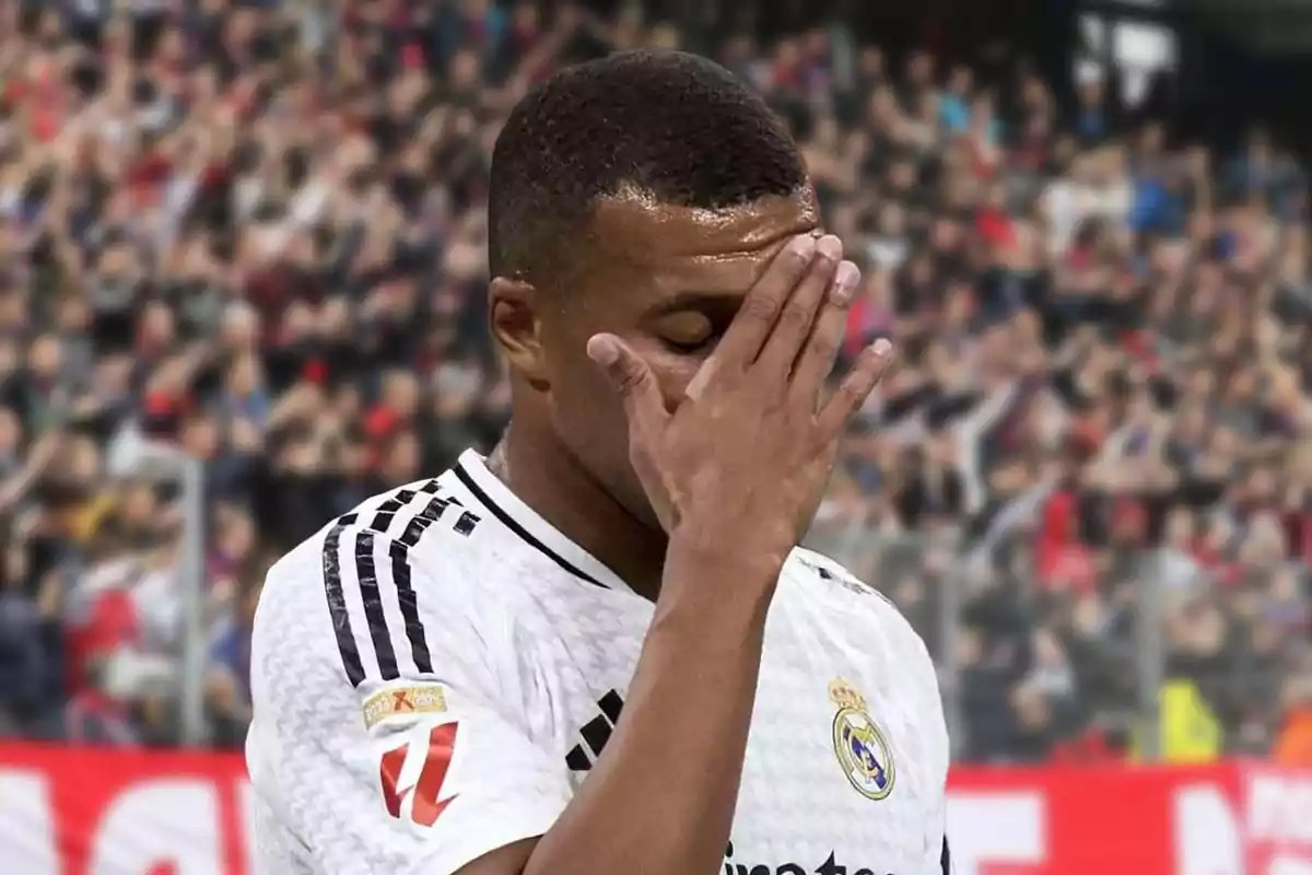 Un jugador de fútbol con la mano en la cara, vistiendo una camiseta blanca con el escudo del Real Madrid, en un estadio lleno de espectadores.