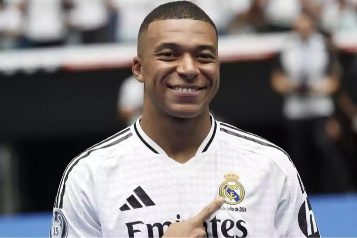 A smiling man wearing a white soccer jersey with the Real Madrid crest on it.