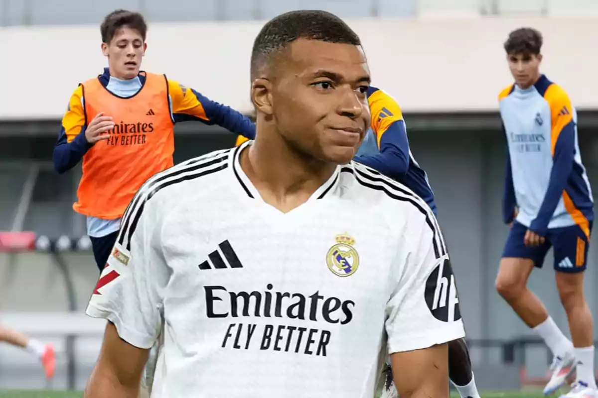 Un jugador de fútbol con camiseta blanca del Real Madrid en primer plano y otros jugadores entrenando al fondo.