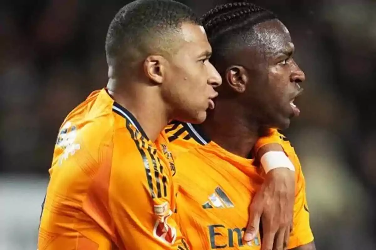 Dos futbolistas con uniforme naranja celebran juntos en el campo.