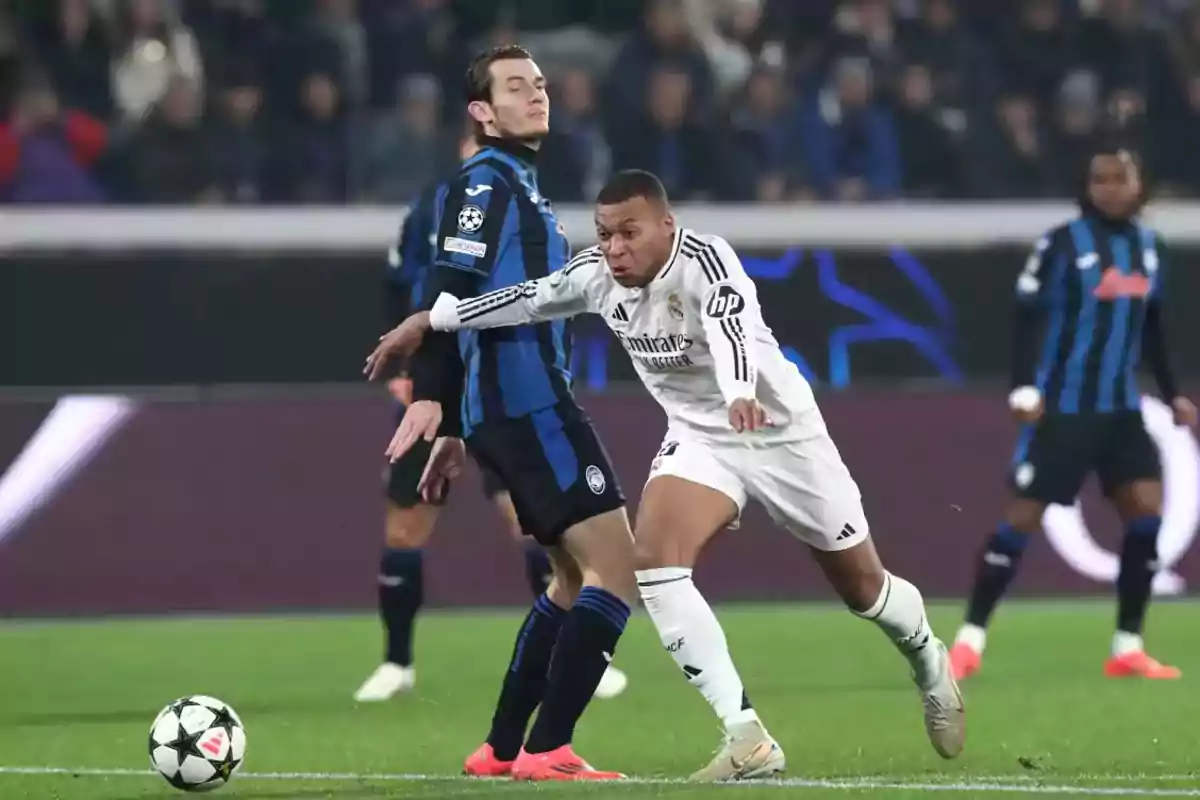 Two soccer players compete for the ball in a game, one wearing a white uniform and the other wearing a blue and black uniform. Two soccer players compete for the ball in a game, one wearing a white uniform and the other wearing a blue and black uniform.