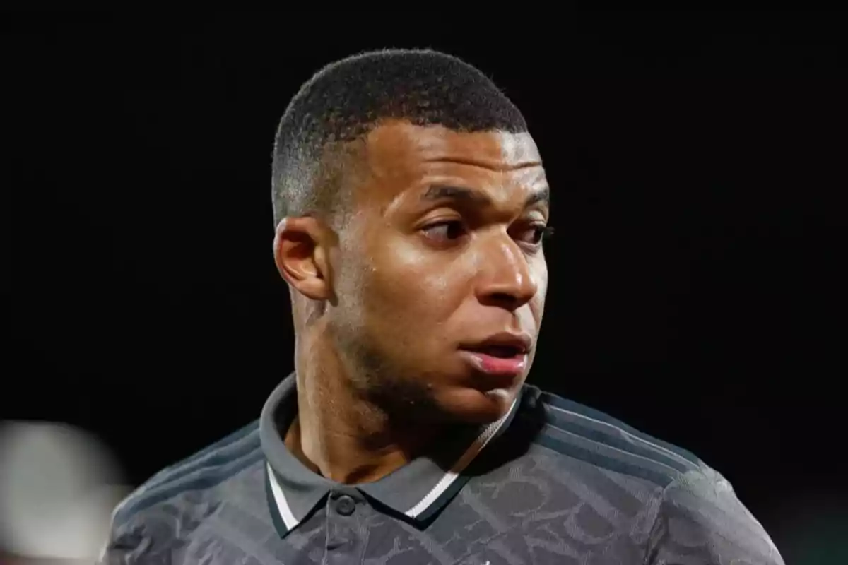 A man in a gray sports jersey looks to the side against a dark background.