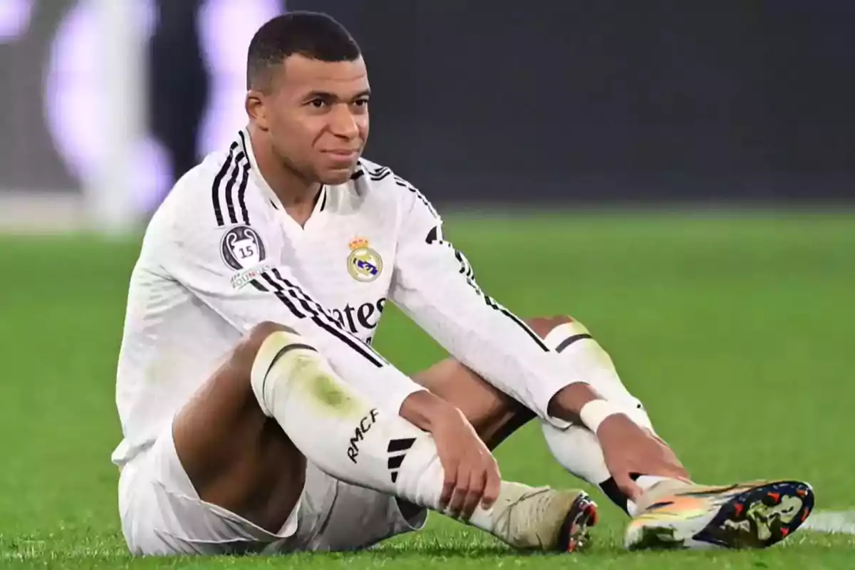 A soccer player in a white uniform is sitting on the playing field.