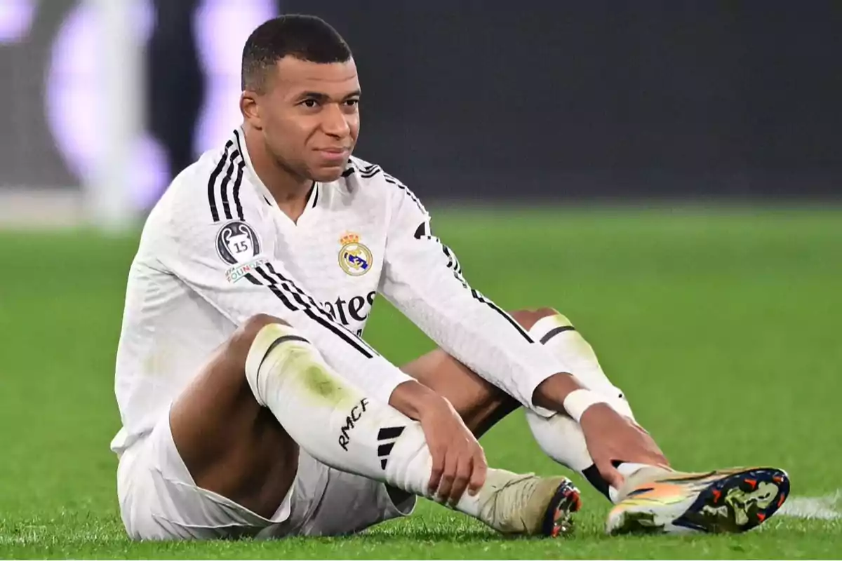 A soccer player in a white uniform sitting on the playing field.