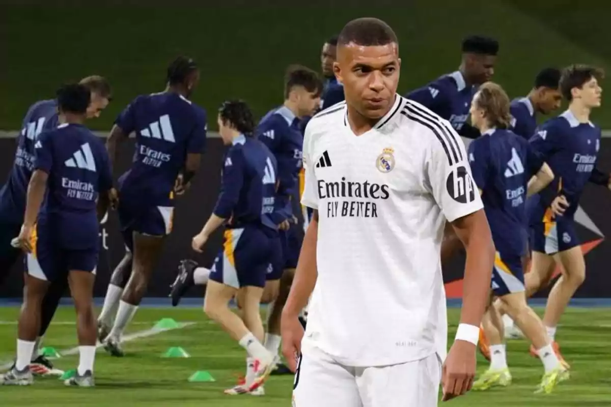 A soccer player in a white uniform in the foreground while other players train in the background.