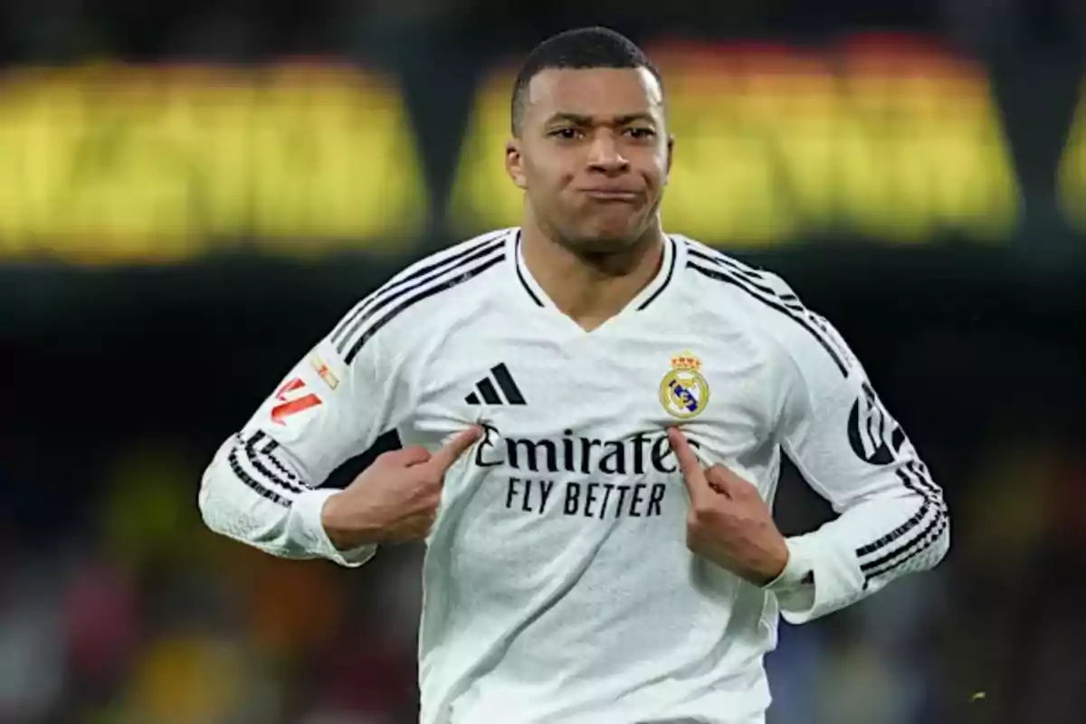 Soccer player in a white Real Madrid uniform pointing to the team’s crest on his jersey during a match