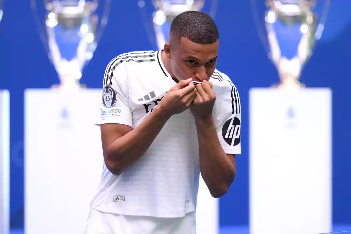 Futbolista besando el escudo de su camiseta blanca durante una presentación con trofeos de fondo Futbolista besando el escudo de su camiseta blanca durante una presentación con trofeos de fondo