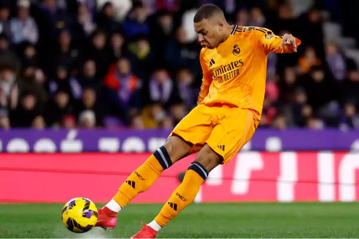 Jugador de fútbol con uniforme naranja pateando un balón en un estadio.