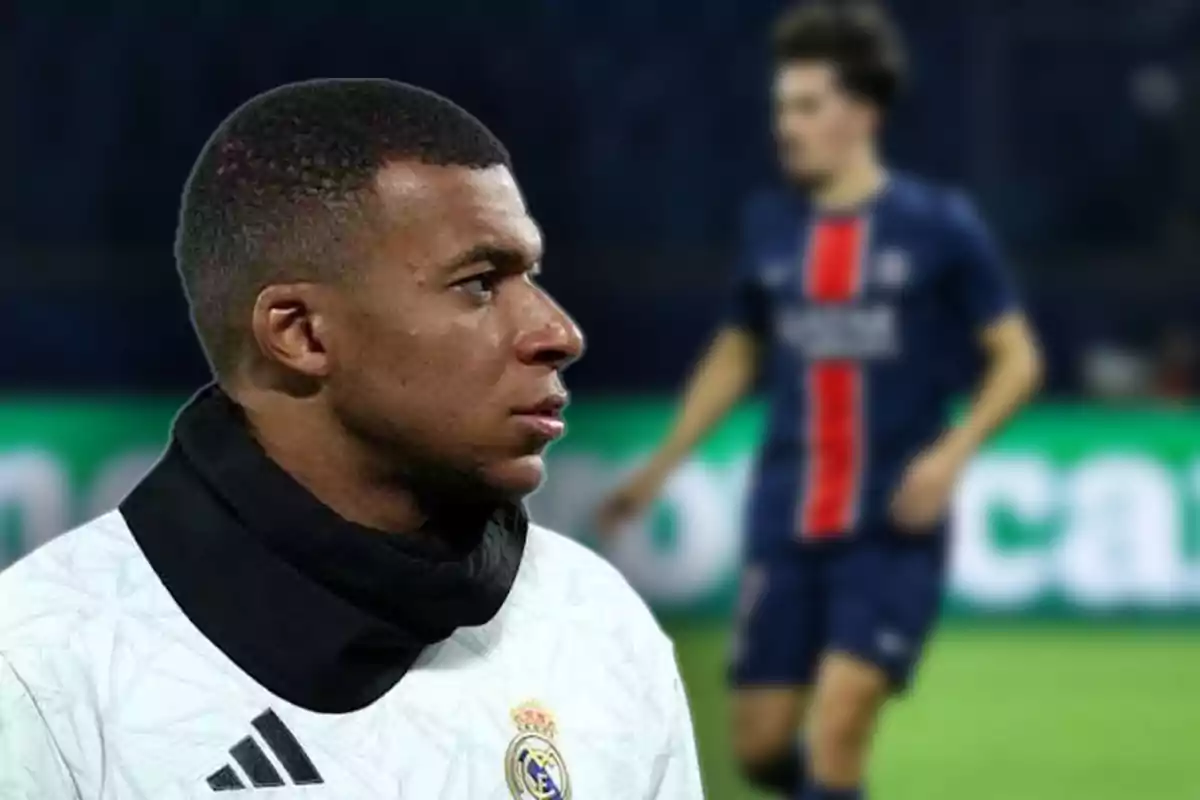 A football player wearing a white jersey with a crest on his chest is in the foreground while another player wearing a blue and red jersey is out of focus in the background.