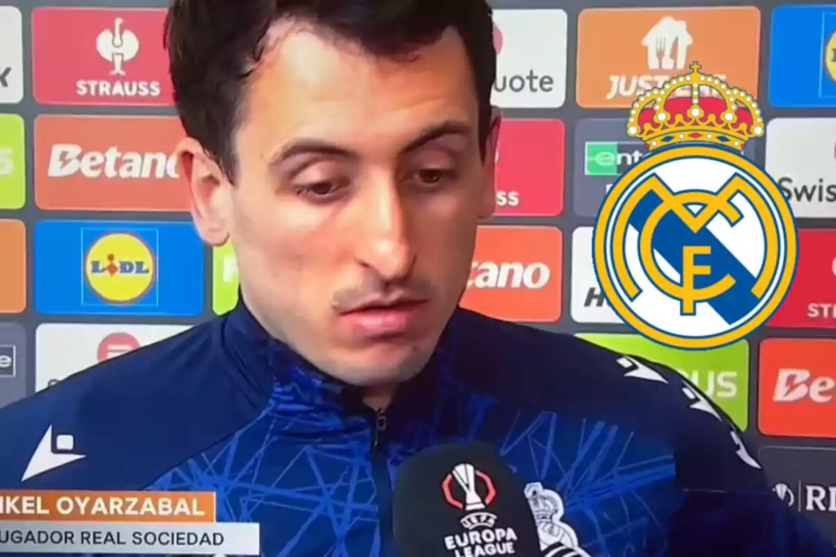 Un jugador de fútbol está siendo entrevistado frente a un fondo con logotipos de patrocinadores y el escudo del Real Madrid aparece superpuesto a la derecha.