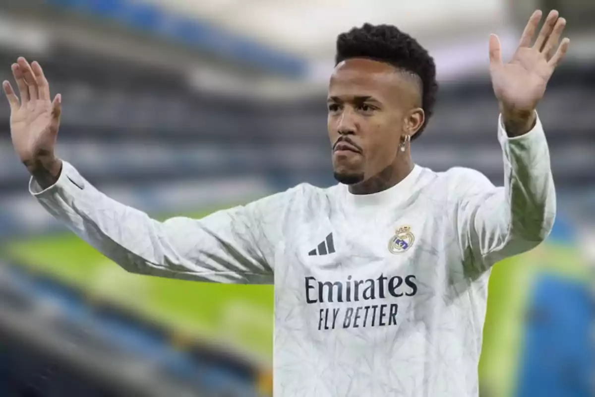 Un jugador de fútbol con uniforme blanco levanta las manos en un estadio.