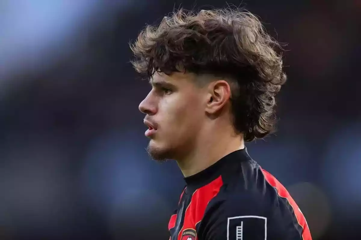 Un jugador de fútbol con cabello rizado y uniforme negro con rojo visto de perfil. Un jugador de fútbol con cabello rizado y uniforme negro con rojo visto de perfil.