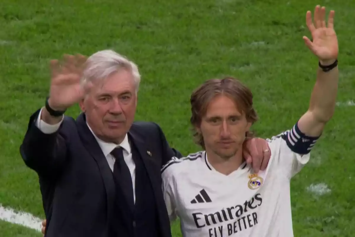 Two people on a soccer field raising their hands in greeting.