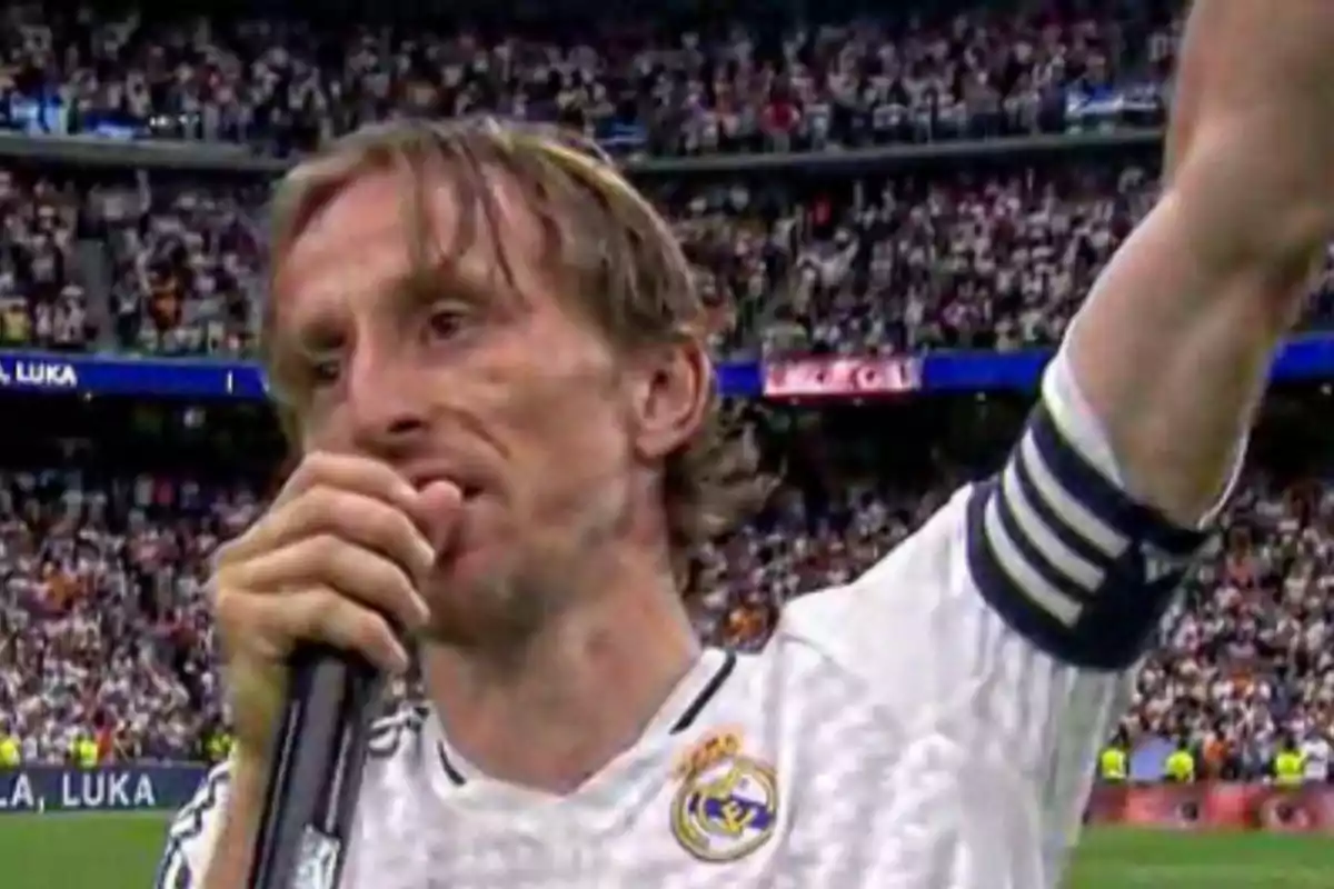 Futbolista con uniforme blanco y brazalete de capitán hablando al micrófono en un estadio lleno de aficionados Futbolista con uniforme blanco y brazalete de capitán hablando al micrófono en un estadio lleno de aficionados