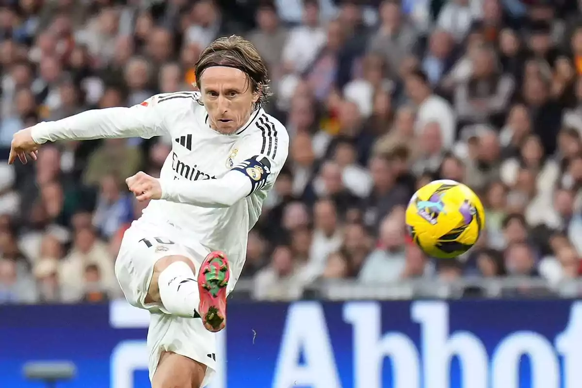 A player in a white uniform kicks a ball in a stadium full of spectators. A player in a white uniform kicks a ball in a stadium full of spectators.