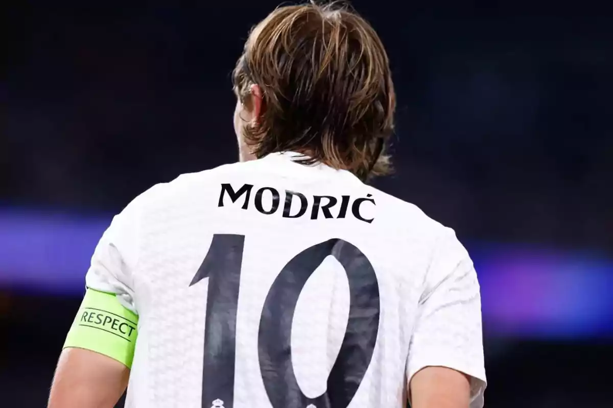 Jugador de fútbol visto de espaldas con el nombre Modric y el número 10 en su camiseta blanca y un brazalete verde en el brazo izquierdo Jugador de fútbol visto de espaldas con el nombre Modric y el número 10 en su camiseta blanca y un brazalete verde en el brazo izquierdo