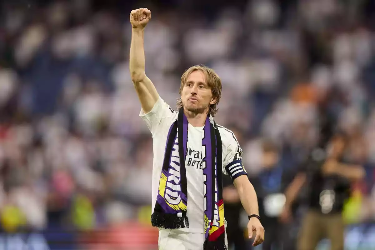 Soccer player in a white uniform and scarf raising his fist in celebration in a stadium full of fans