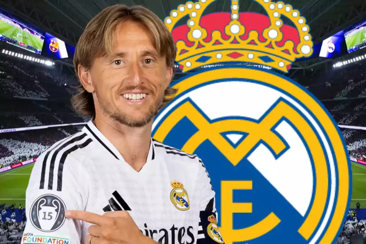 Un jugador de fútbol con la camiseta del Real Madrid sonríe mientras señala un parche en su manga, con el escudo del club y un estadio de fondo.