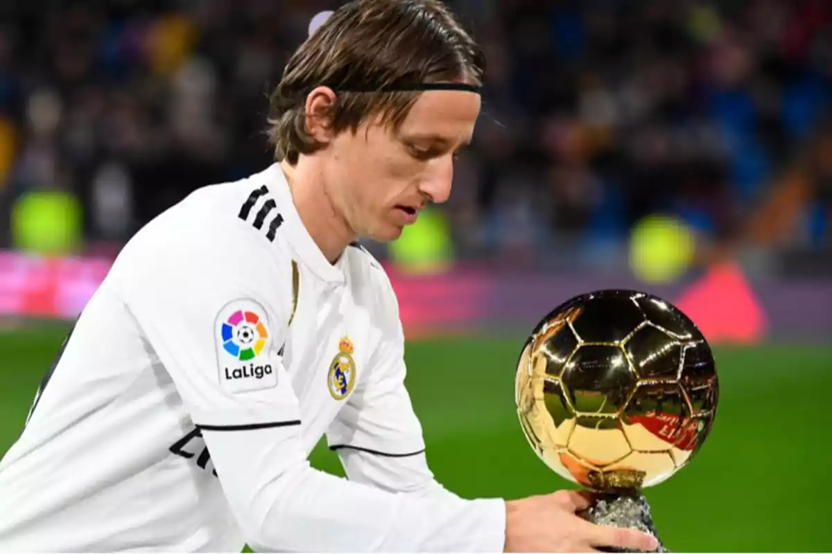 Jugador de fútbol con uniforme blanco sosteniendo un trofeo dorado en un estadio. Jugador de fútbol con uniforme blanco sosteniendo un trofeo dorado en un estadio.