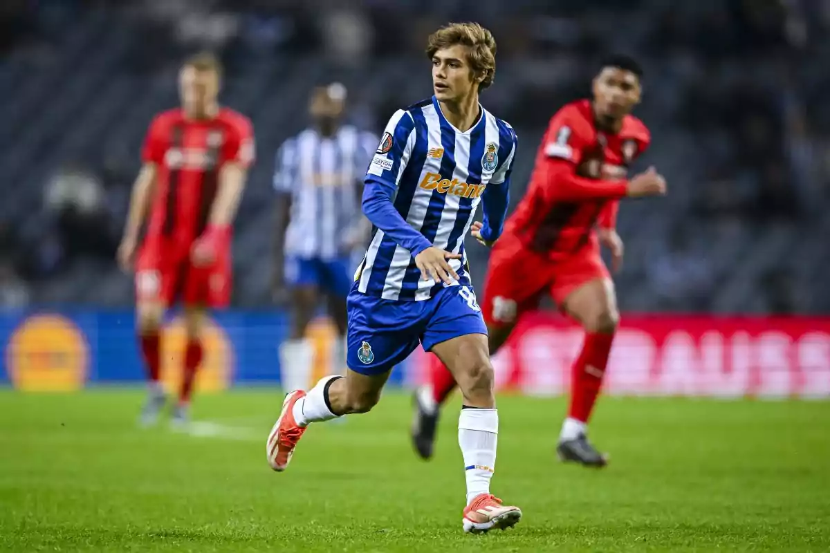 A player in a blue and white uniform runs on the field during a match, while other players in red uniforms are in the background. A player in a blue and white uniform runs on the field during a match, while other players in red uniforms are in the background.