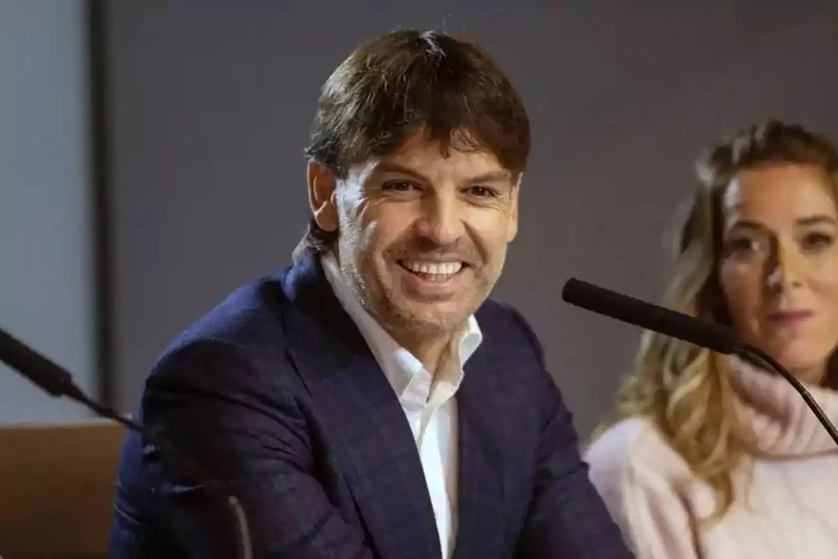 A smiling man at a press conference next to a woman. A smiling man at a press conference next to a woman.