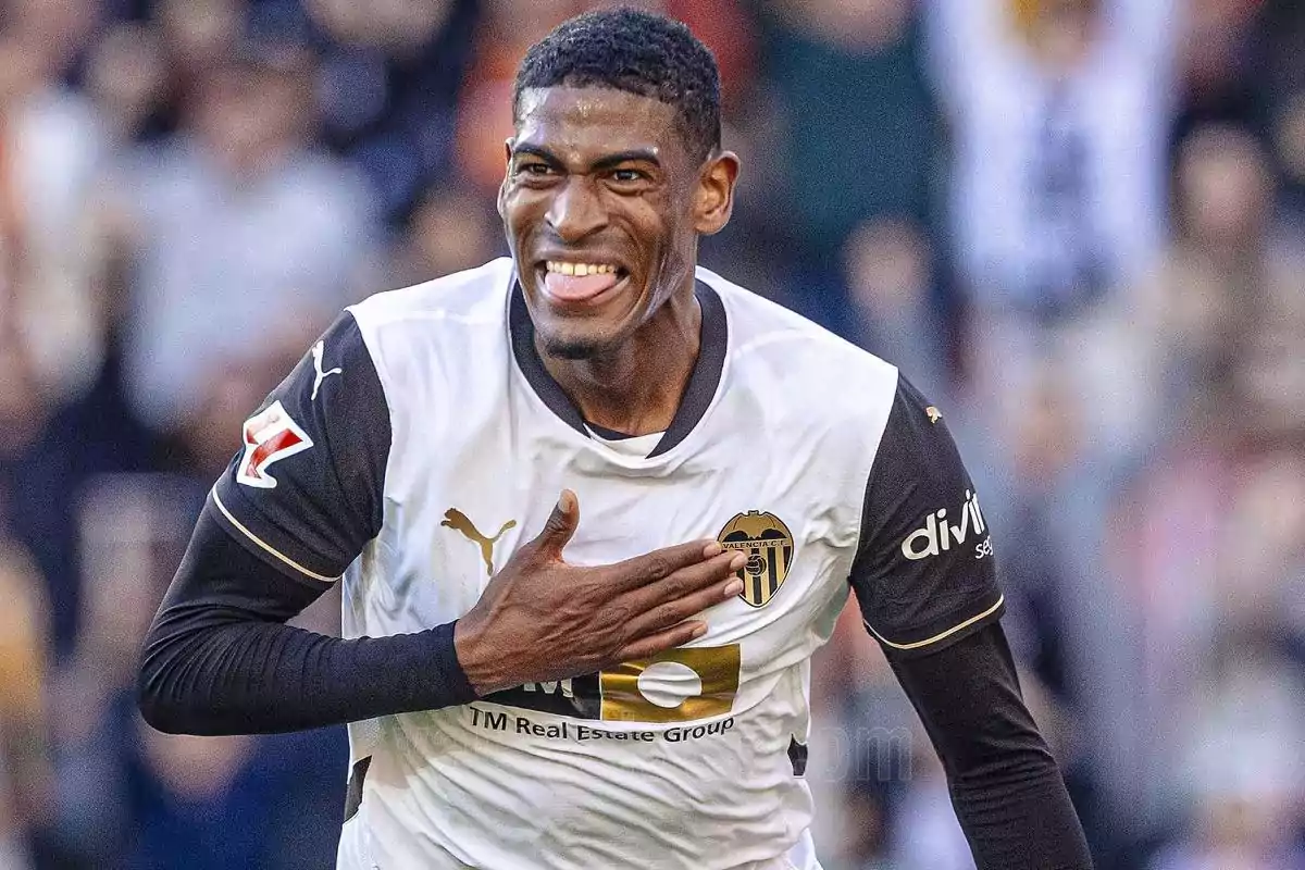 Un jugador de fútbol sonríe mientras se lleva la mano al pecho vistiendo el uniforme del Valencia CF. Un jugador de fútbol sonríe mientras se lleva la mano al pecho vistiendo el uniforme del Valencia CF.