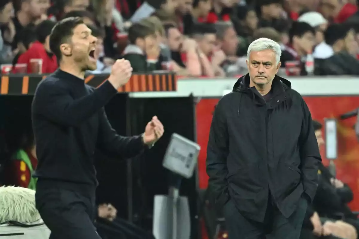 Two soccer coaches on the sideline, one gesturing enthusiastically while the other watches with a serious expression, with a background of spectators in the stands. Two soccer coaches on the sideline, one gesturing enthusiastically while the other watches with a serious expression, with a background of spectators in the stands.
