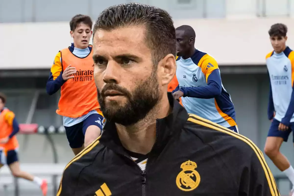 Un jugador de fútbol del Real Madrid en primer plano con otros jugadores entrenando al fondo.