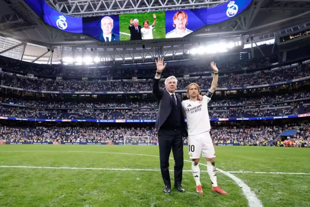 Two people in a soccer stadium wave to the crowd while their images are displayed on the giant screen. Two people in a soccer stadium wave to the crowd while their images are displayed on the giant screen.